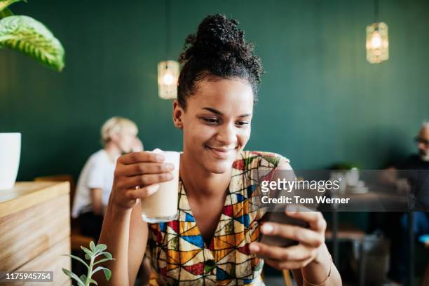young woman drinking latte and looking at smartphone - coffee chat stockfoto's en -beelden
