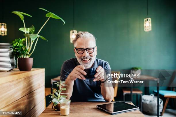 portrait of cafe customer smiling while drinking coffee - uomini maturi foto e immagini stock