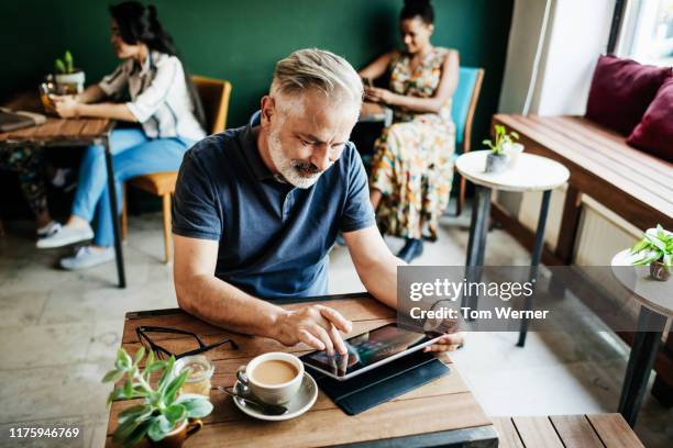 mature man using digital tablet in cafe - mature man using digital tablet stock pictures, royalty-free photos & images