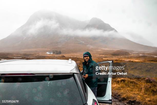 happy guy in a adventure off road with car in the scottish highlands with rain. - scottish coat stock pictures, royalty-free photos & images