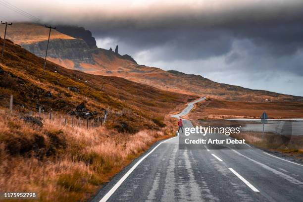 guy with red raincoat in the road with the landscape of the skye island. - old man of storr stock pictures, royalty-free photos & images