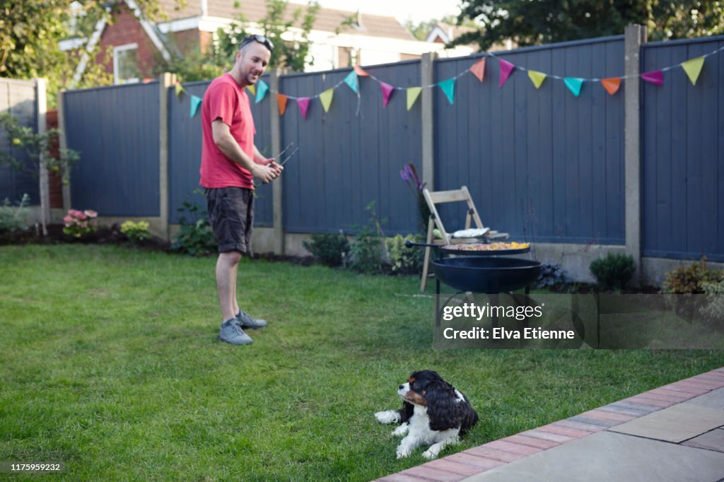 Pet dog trying to ignore man barbecueing food in the background