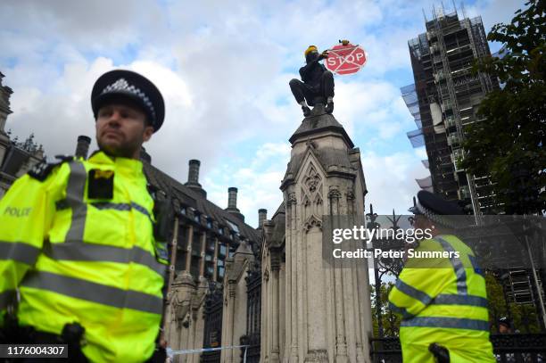 Climate change protester wearing a gas mask and holding a STOP sign sits on the fence around the Houses of Parliament on October 15, 2019 in London,...