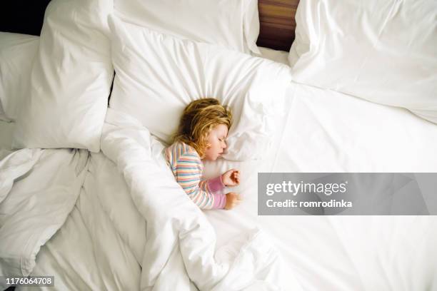 Cute little toddler girl sleeping in big bed of parents. Adorable baby child dreaming in hotel bed on family vacations or at home.