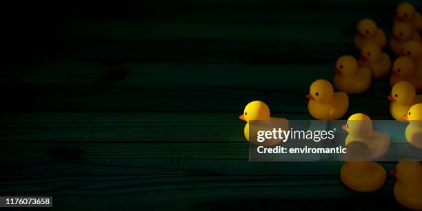 yellow rubber ducks in a group following one leader duck heading towards a shaft of light shining through the darkness, scene set on an old turquoise colored weathered wooden panel background, conceptually representing water. - ducks following stock pictures, royalty-free photos & images