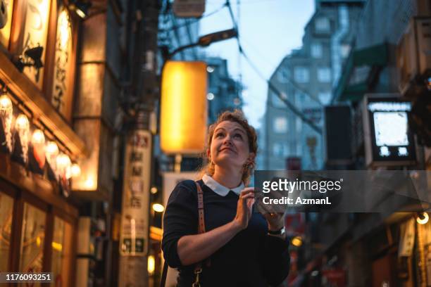 caucasian woman using smart phone to navigate tokyo at night - japan tourism stock pictures, royalty-free photos & images