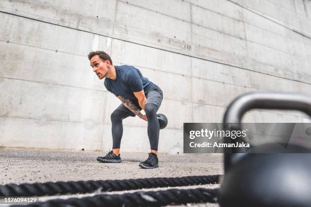crouching männliche athlet tun doppelhanded kettlebell swing - kugelhantel stock-fotos und bilder