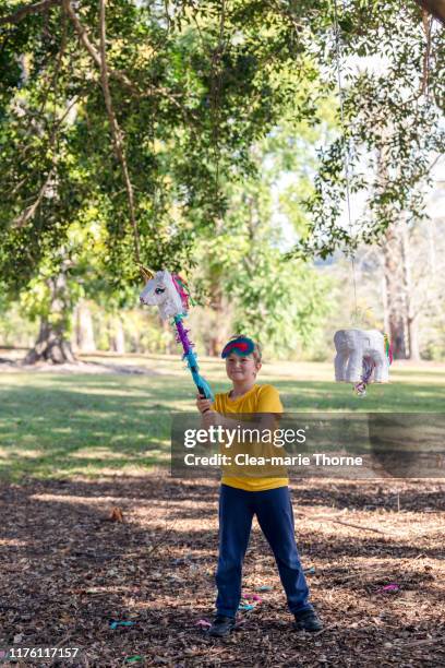 young child playing hit the pinata in a park on a sunny day. - einhorn wald stock-fotos und bilder