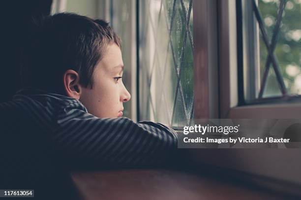 young boy looking out window on rainy day - sad boy stock-fotos und bilder