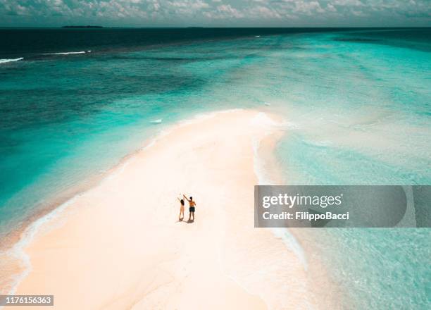 giovane coppia adulta in piedi su un banco di sabbia contro l'acqua turchese alle maldive - viaggio di nozze foto e immagini stock