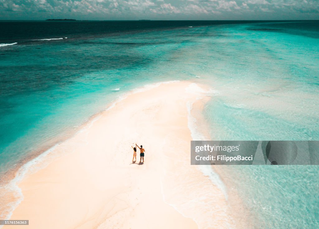 Young adult couple standing on a sandbank against turquoise water in Maldives