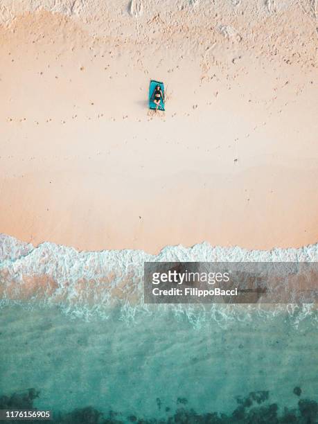 giovane donna adulta sdraiata su una spiaggia paradisiaca contro l'acqua turchese alle maldive al tramonto - telo da mare foto e immagini stock