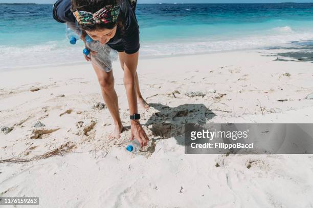 giovane donna adulta che raccoglie alcune bottiglie di plastica abbandonate sulla spiaggia - pick foto e immagini stock