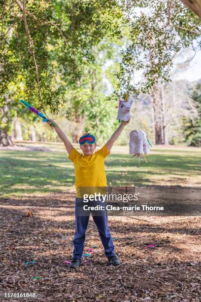 young child playing hit the pinata in a park on a sunny day. - einhorn wald stock-fotos und bilder
