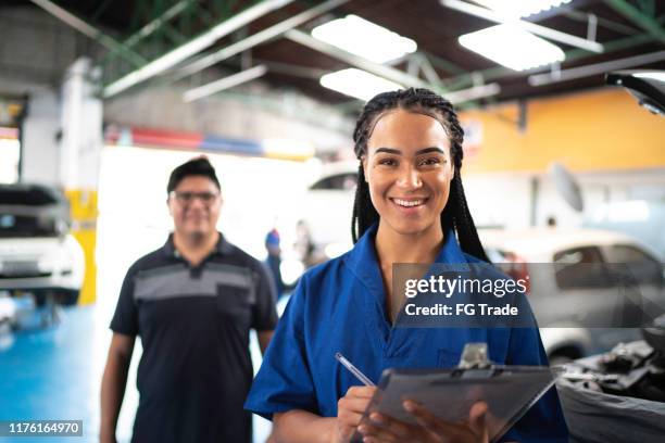 retrato de mujer mecánica automotriz con el cliente en el fondo en el taller de reparación de automóviles - car mechanic fotografías e imágenes de stock