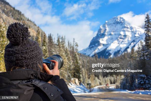 Over the shoulder portrait of a woman taking pictures of mountains around Banff National Park in Alberta, Canada, taken on December 4 2018.