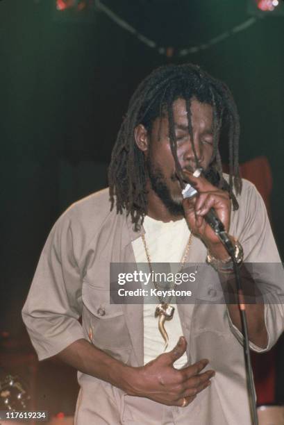 Peter Tosh , Jamaican reggae musician and singer, singing into a microphone during a live concert performance, circa 1985. Tosh was a member of the...