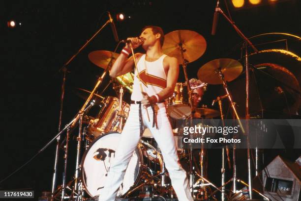 Freddie Mercury , singer with Queen, standing in front of a drumkit as he sings into a microphone on stage during a live concert performance by the...