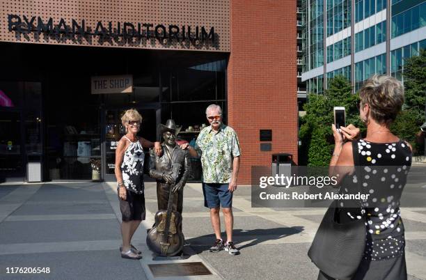 Tourists take souvenir photographs beside a bronze statue of country music singer Little Jimmy Dickens in front of the Ryman Auditorium in Nashville,...
