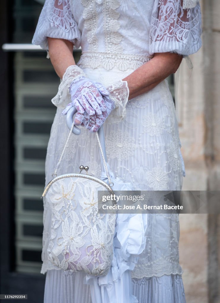 Hands of a woman with a handbag and umbrella in a modernist period costume.