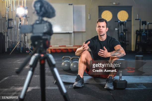 atleta masculino sentado en la alfombra de ejercicio y haciendo vlog en el gimnasio - instructor de acondicionamiento físico fotografías e imágenes de stock