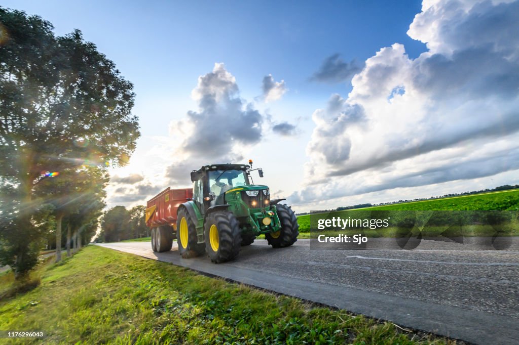 Trattore John Deere che trasporta un rimorchio ribaltabile su una strada di campagna tra i campi agricoli