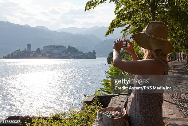 woman takes picture across lake to distant island - lake orta stock pictures, royalty-free photos & images