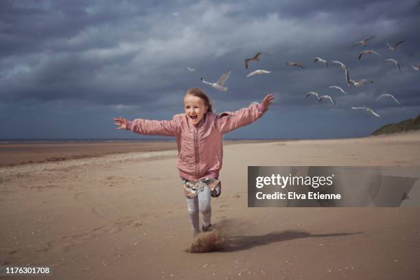 young happy girl (6-7) running on a beach in england chased by seagulls - chasing stock pictures, royalty-free photos & images