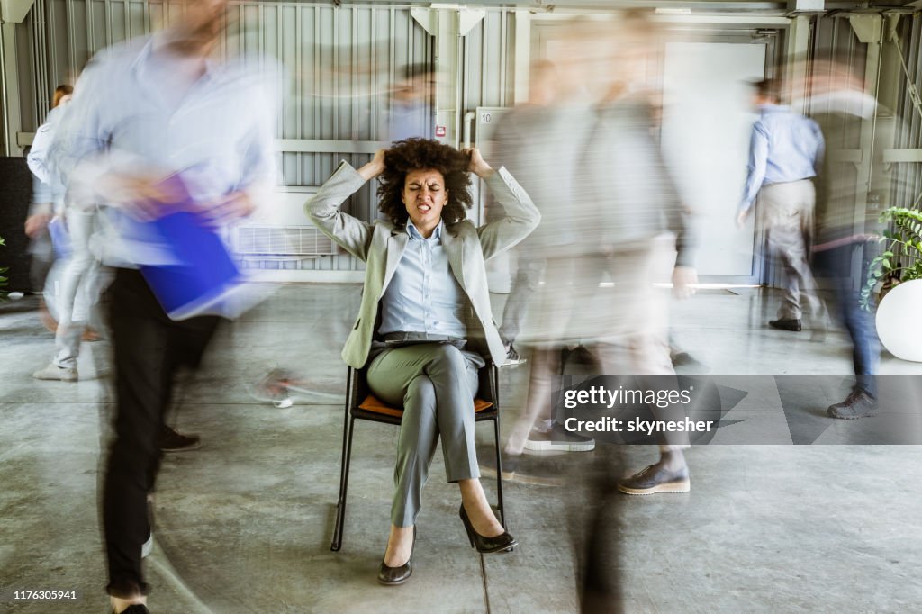 Frustrated African American businesswoman surrounded by her colleagues in blurred motion.