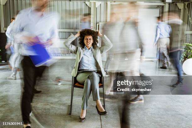 frustrated african american businesswoman surrounded by her colleagues in blurred motion. - compression imagens e fotografias de stock