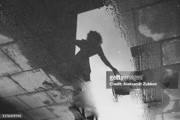 reflection of a girl with a bag in her hand in a puddle on a stone pavement. black and white - soul city ストックフォトと画像