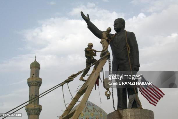 Marines chain the head of a statue of Saddam Hussein before pulling it down in Baghdad's al-Fardous square 09 April 2003, while an Iraqi waves the US...
