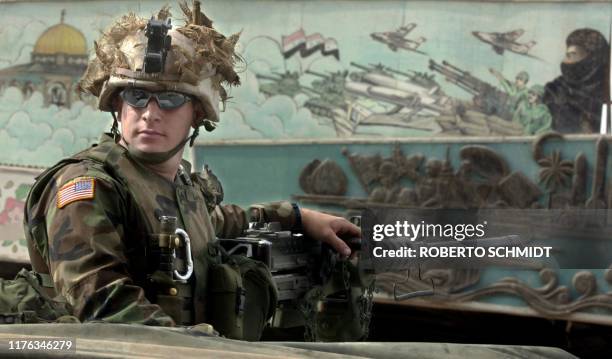 Army Sergeant Callihan sits atop a humvee in his unit's base next to a 50 caliber machine gun in front of a mural depicting Iraqi army marching...