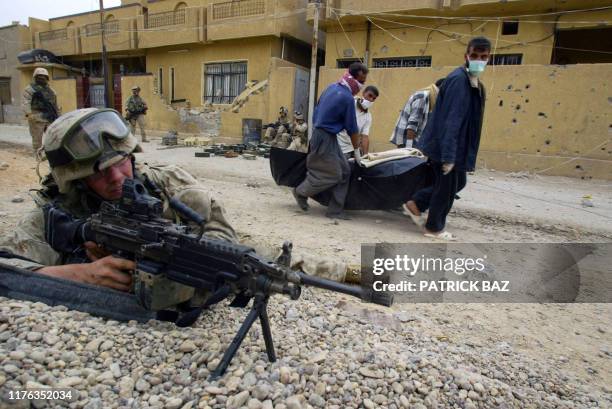 Iraqi volunteers carry a dead body past a US marine with 3/5 marines Kilo company in the city of Fallujah 17 November 2004. Eleven bodies were...