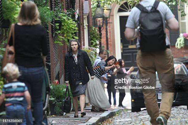 Tourists take photographs on Acorn Street in Boston, as a woman who entered one of the residences passes through them on the sidewalk, on Oct. 7,...