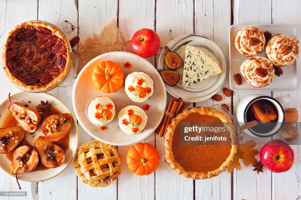 Autumn food table scene with pies, appetizers and desserts. Top view over a white wood background.