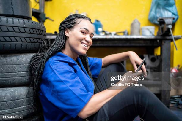 female mechanic relaxing using mobile at break in a auto repair shop - stereotypically working class stock pictures, royalty-free photos & images
