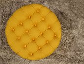 Top view of round fabric yellow pouf with buttons and squares. Gray carpet background