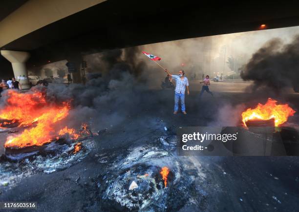 Lebanese demonstrator waves the national flag next to a tire fire during a protest against dire economic conditions in the Lebanese capital Beirut's...