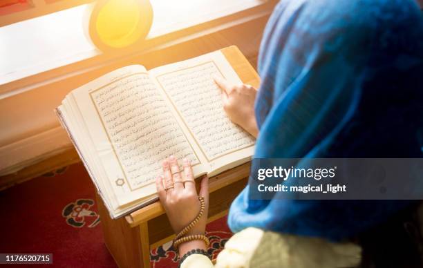 praying young muslim woman. middle eastern girl praying and reading the holy quran. muslim woman studying the quran at the mosque - koran stock pictures, royalty-free photos & images