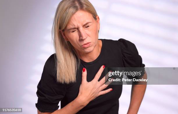 adult woman clutching heart in pain - cardiopatía fotografías e imágenes de stock