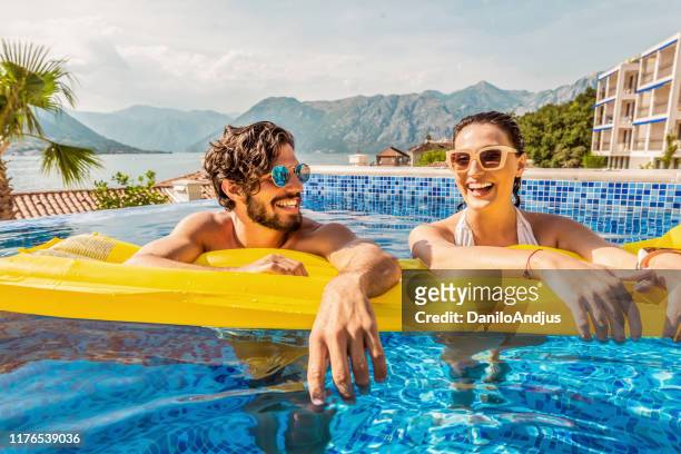 verspieltes paar lächelnd in einem pool - luftmatratze stock-fotos und bilder