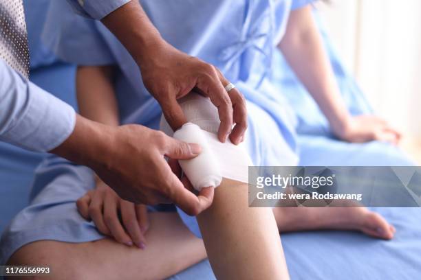 close up hand of doctor wrapping a bandage to the knee of patients - accident recovery stockfoto's en -beelden