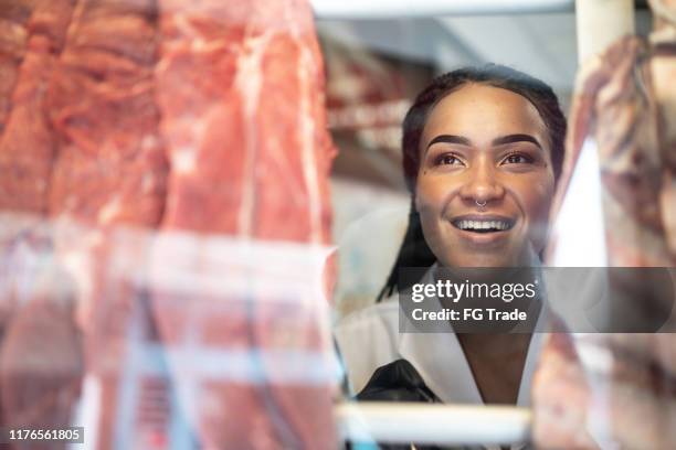 young butcher looking through meat display - meat factory stock pictures, royalty-free photos & images