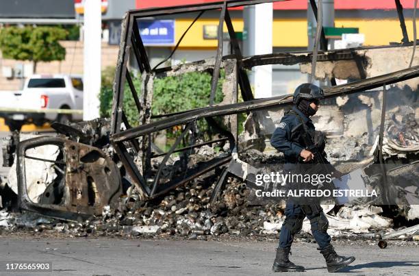 Policeman walks past a burnt vehicle after heavily armed gunmen waged an all-out battle against Mexican security forces in Culiacan, Sinaloa state,...