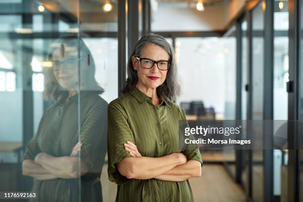 confident mature businesswoman with arms crossed - dreiviertelansicht stock-fotos und bilder