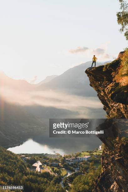 one person standing on top of a cliff over geiranger, norway - geiranger stock-fotos und bilder