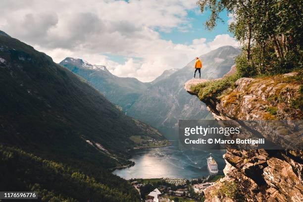 one person standing on top of a cliff over geiranger, norway - majestätisch stock-fotos und bilder