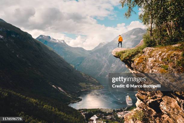 one person standing on top of a cliff over geiranger, norway - conviction stockfoto's en -beelden