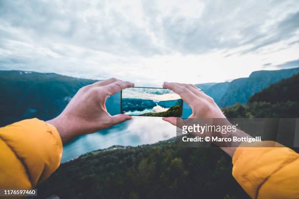 personal perspective of man photographing a norwegian fjord with smartphone, norway - fotografia foto e immagini stock